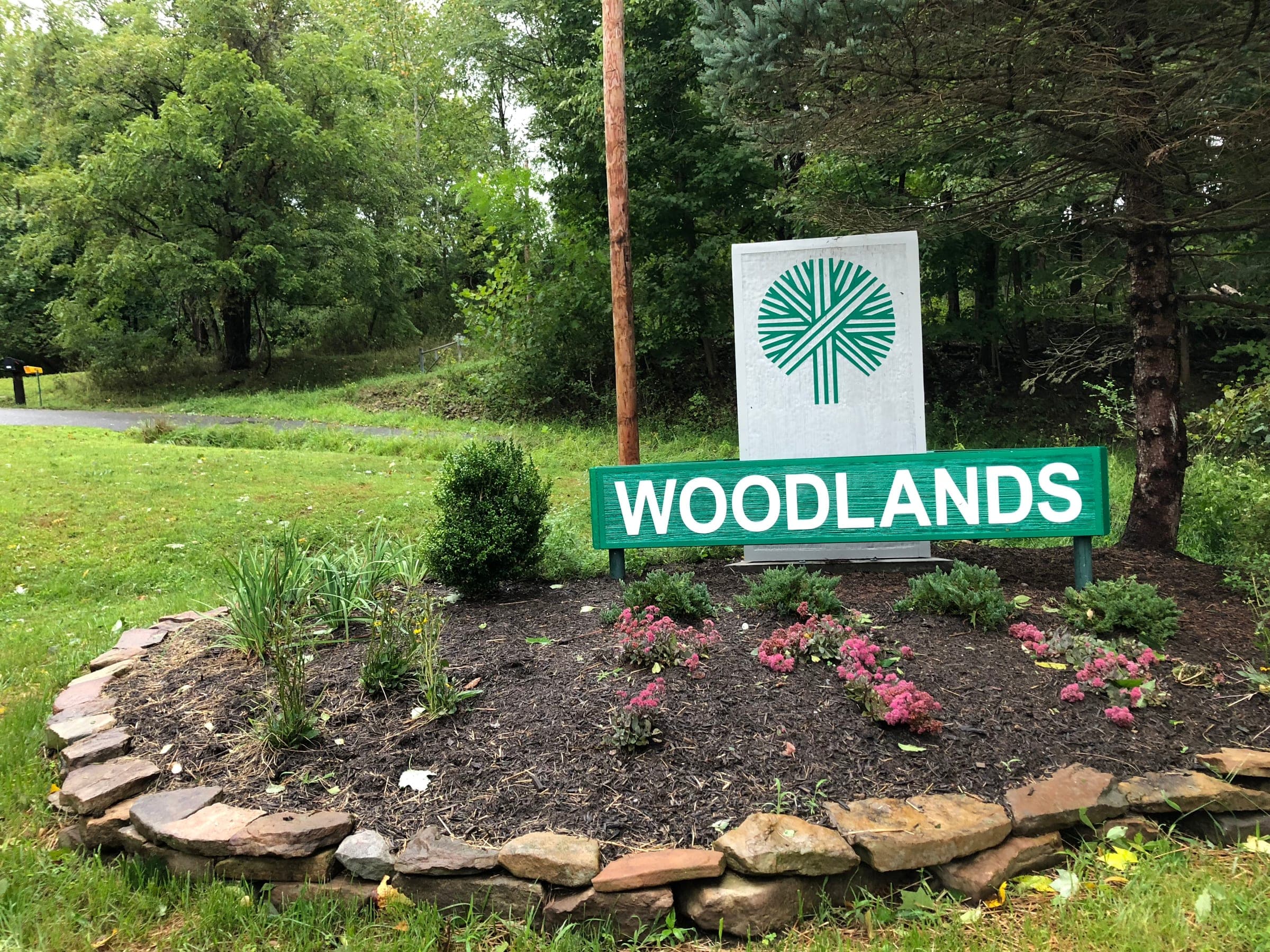 Green and white sandblasted Woodlands entrance sign in a landscaped stone bed